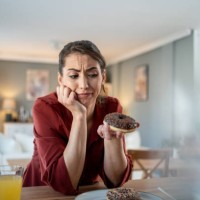 woman feeling guilty while eating chocolate donut at home - junk food stock pictures, royalty-free photos & images
