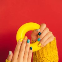 woman hands with bright manicure and in yellow knitted sweater are holding illuminating yellow bagel against red background. trendy colors of the year 2021. front view. copy space for your design - nails art stock pictures, r