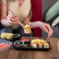 woman having takeaway or delivery sushi rolls meal from a plastic package with sauces at home - junk food stock pictures, royalty-free photos & images