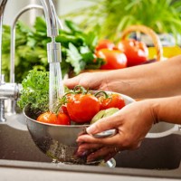 woman holding a colander full of fresh vegetables under running water in kitchen sink - food stock pictures, royalty-free photos & images