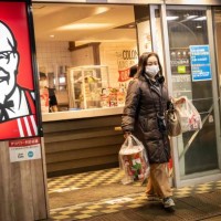 Woman holding Christmas meal boxes leaves a KFC restaurant on Christmas Eve in Tokyo on December 24, 2022. - Forget turkey, stuffing and brussels...