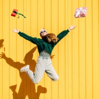 woman in christmas hat and green sweater jumping with christmas gift box against the yellow wall. - fashion stock pictures, royalty-free photos & images