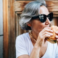 woman in sunglasses eating burger while sitting against door - junk food stock pictures, royalty-free photos & images