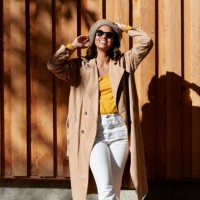 woman in trench coat raising arms in front of wooden wall - fashion stock-fotos und bilder
