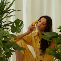 woman in yellow jumpsuit talking on yellow retro phone, sitting amount large monstera plants. - fashion stock pictures, royalty-free photos & images