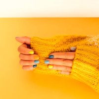 woman in yellow white knitted sweater is demonstrating her hands with bright multi colored manicure above yellow table. trendy colors of the year 2021 - nails art stock pictures, royalty-free photos & images