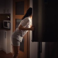 woman leaning into fridge at night searching for food with bad diet habits. - junk food stock pictures, royalty-free photos & images