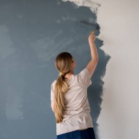 woman painting a wall of her new house with a blue or grey color - home decoration stock pictures, royalty-free photos & images