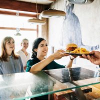 woman picking up burger from restaurant counter - junk food stock pictures, royalty-free photos & images