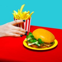 woman picking up french fries near burger on table against blue background - junk food stock pictures, royalty-free photos & images