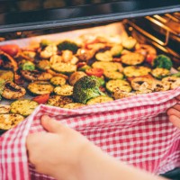 woman putting a tray of vegetables in the oven. - food stock pictures, royalty-free photos & images