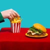 woman reaching for french fries near cheeseburger on table against blue background - junk food stock pictures, royalty-free photos & images