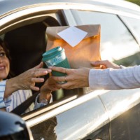 woman receiving a cup of coffee and takeaway food at the drive through - junk food stock pictures, royalty-free photos & images