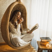 woman relaxing at home in hanging ball chair, reading book and drinking hot herbal tea - home decoration stock pictures, royalty-free photos & images
