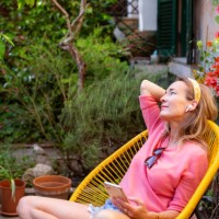 woman relaxing in garden chair, holding smartphone - garden decoration photos et images de collection