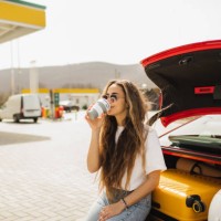 woman relaxing with coffee on the road trip. coffee break on gas station, sitting on car boot. - junk food stock pictures, royalty-free photos & images