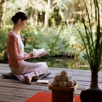 woman sits on a cushion in her garden reading a book - garden decoration stockfoto's en -beelden