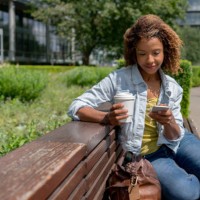 woman sitting on a bench outdoors social networking on her phone - junk food stock pictures, royalty-free photos & images