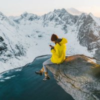 woman sitting on cliff and using smartphone on lofoten island in snow - travel stock pictures, royalty-free photos & images