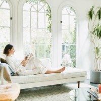 woman sitting on couch in living room reading on digital tablet - fashion photos et images de collection
