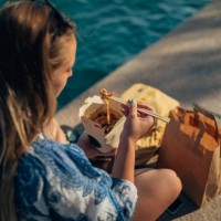 woman uses chopsticks to eat chinese takeout food by the sea - junk food stock pictures, royalty-free photos & images