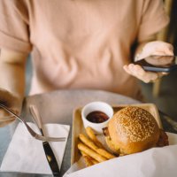 woman using smartphone while having meal in a restaurant - junk food stock pictures, royalty-free photos & images