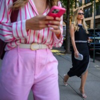 Woman wearing a black dress with silver trim with a silver purse and sandel high heels walks near a woman on her phone outside Pat Bo during the New...