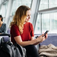 woman wearing red using smartphone while waiting for a flight - travel stock pictures, royalty-free photos & images