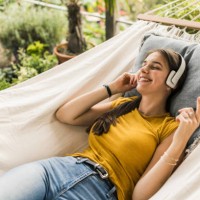 woman with eyes closed listening music through headphones while relaxing on hammock in yard - garden decoration photos et images de collection
