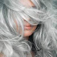 woman with grey hair blowing across her face. - hairstyle stock-fotos und bilder
