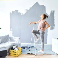 woman with hand on hip leaning on ladder while standing against wall at home - home decoration stock pictures, royalty-free photos & images
