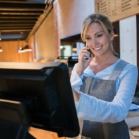 woman working at a bakery talking to a customer on smartphone and registering the takeout on the system - junk food stock pictures, royalty-free photos & images