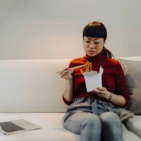 woman working on laptop and eating pasta while sitting on sofa - junk food stock pictures, royalty-free photos & images