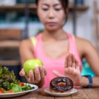 women push the donut plate that is a mixture of trans fat. and choose to hold the apple. don't eat junk food. diet concept - junk food stock pictures, royalty-free photos & images