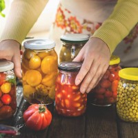 women with traditional apron holding jars with various pickled preserved vegetables on rustic, wooden kitchen table. - food stock pictures, royalty-free photos & images