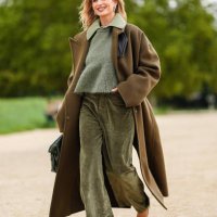 Xenia Adonts wears light green buttoned up long sleeve Loewe shirt, dark green Loewe sweater, dark green velvet Loewe pants, dark green Loewe coat,...