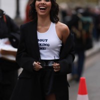 Xochitl Gomez is seen wearing an oversized black blazer with peak lapels and shoulder pads, a white tank top with a dark blue printed quote saying...