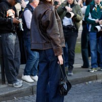 Yasmin Wijnaldum wears brown leather jacket, blue wide leg jeans, Adidas black sneakers, black bag, outside Nina Ricci, during the Womenswear...