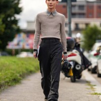 Yoshiaki wears light gray collar light brown gray long sleeve shirt, black high waisted pants, black leather bag with yellow bar charm, shiny black...
