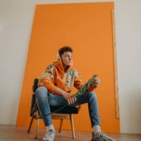 young adult caucasian man sitting and posing in front of orange background. - fashion stock pictures, royalty-free photos & images