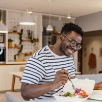 young african-american man eating takeaway meal at home and planning activities - junk food stock pictures, royalty-free photos & images