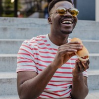 young african-american man is eating hot dog and smiling - junk food stock pictures, royalty-free photos & images