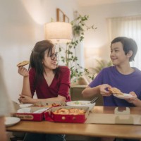 young asian boy sharing his piece of pizza to his mom while they enjoy lunch together on weekend at home. - junk food stock pictures, royalty-free photos & images