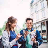 young asian couple enjoying street food together while exploring in vibrant streets of a new city - food stock pictures, royalty-free photos & images