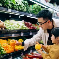 young asian father and her little daughter grocery shopping in supermarket. they are choosing fresh organic bell peppers together along the produce aisle. fruits and vegetables shopping. routine grocery shopping. going green 