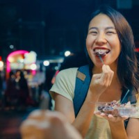 young asian female friends backpacker enjoy eating street food on the street at night market in bangkok, thailand. holiday vacation trip. - food stock pictures, royalty-free photos & images