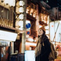 young asian female traveller with backpack visiting japan, exploring and strolling in downtown city street at night in osaka. a popular nightlife and entertainment area in the city. travel, vacation and holiday concept - trav