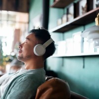 young asian man with eyes closed, enjoying music over headphones while relaxing on the sofa at home - home decoration stock pictures, royalty-free photos & images