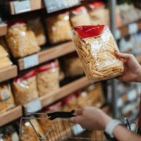 young asian woman carrying a shopping basket, grocery shopping in supermarket, close up of her hand choosing a pack of organic pasta along the aisle. healthy eating lifestyle - food stock pictures, royalty-free photos & image
