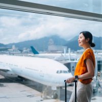 young asian woman carrying suitcase, looking through window at airport terminal while waiting for departure. ready for a trip. business travel. travel and vacation concept - travel photos et images de collection